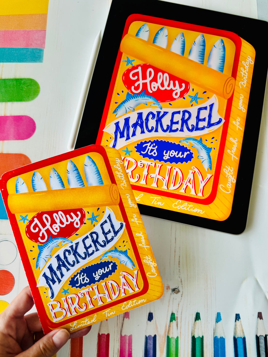 Hand holding the Holly Mackerel birthday card next to an iPad showing the original Procreate illustration, by Be Unique by Romy
