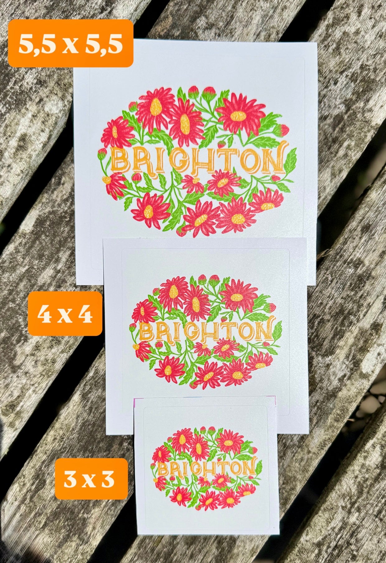 Three decorative stickers with floral designs and 'Brighton' text on a wooden surface.