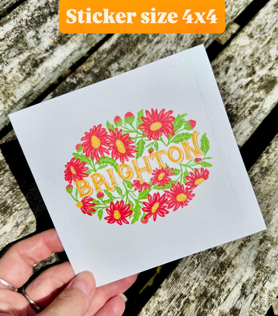 Sticker with floral design and 'Brighton' text held over a wooden surface