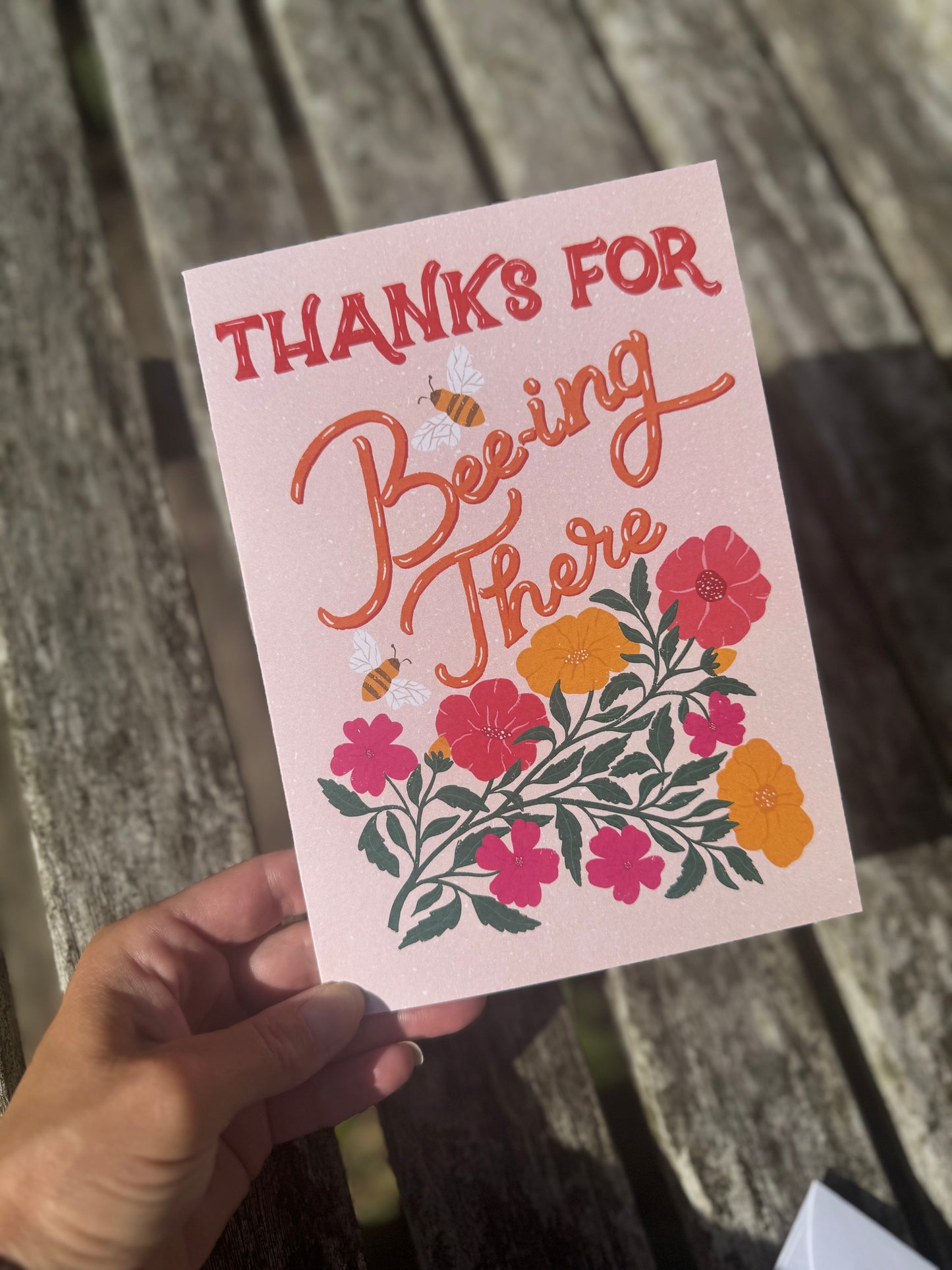 Card with floral design and text held by a hand on a wooden surface