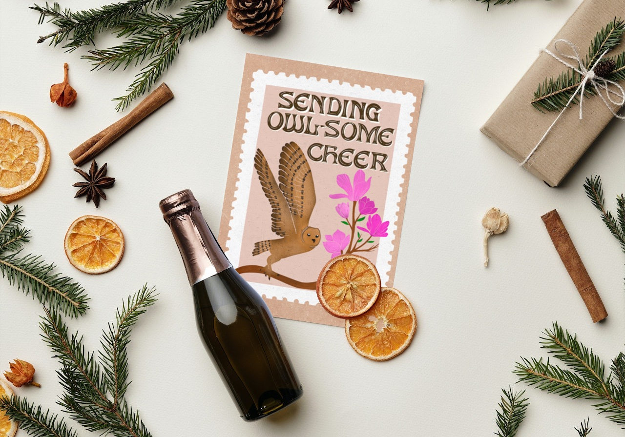 Bottle of champagne, festive card with owl design, and decorative items on a white surface