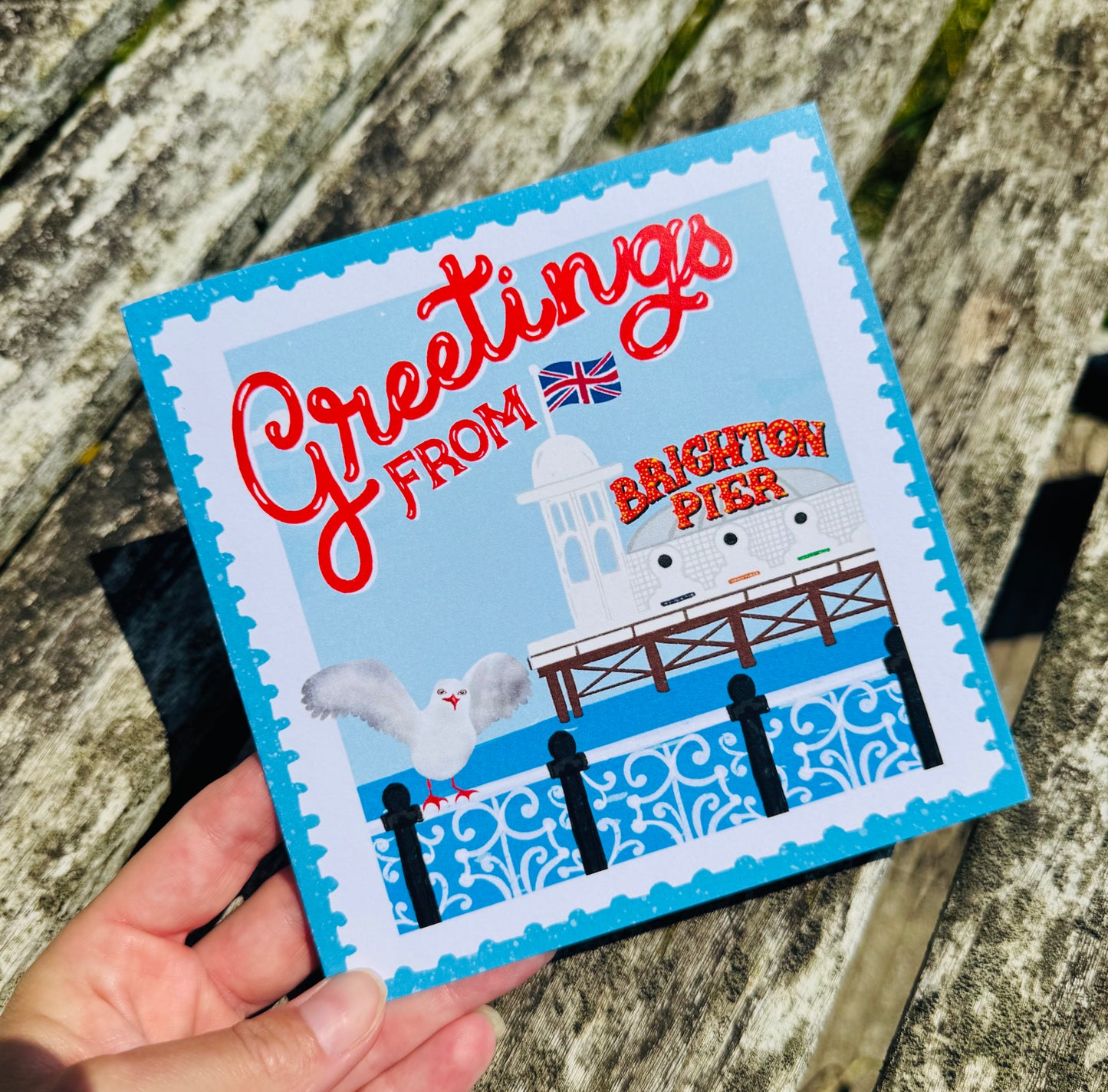 Card with 'Greetings from Brighton Pier' text and illustration on a wooden surface