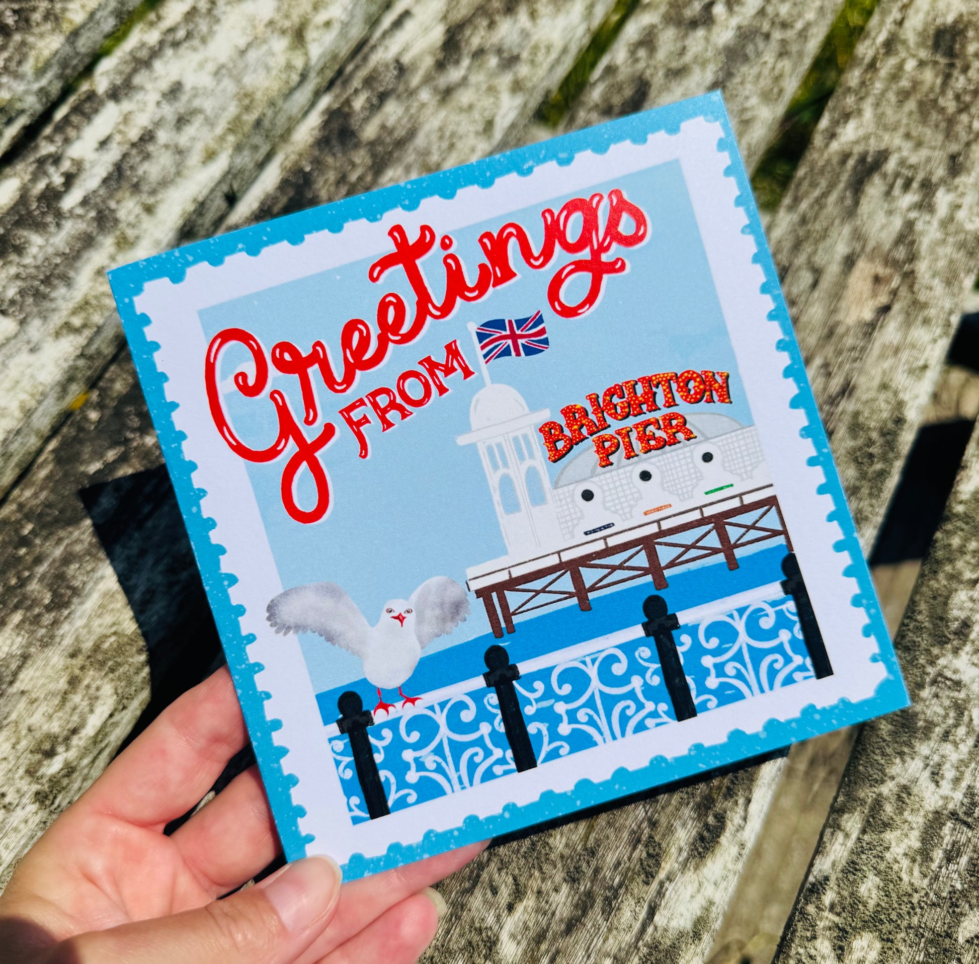 Card with 'Greetings from Brighton Pier' text and illustration on a wooden surface