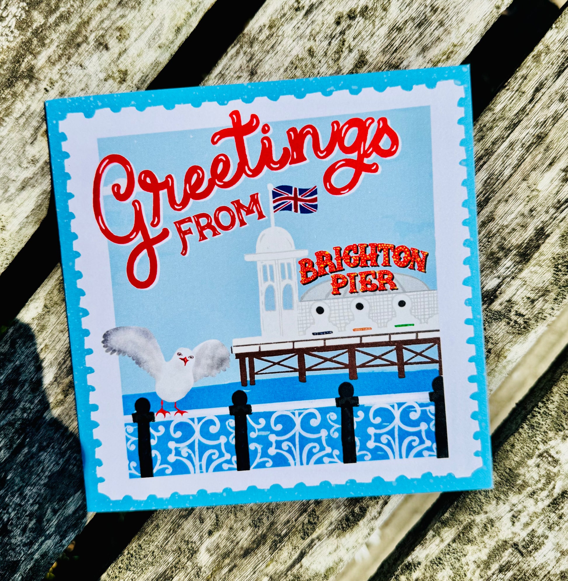 Greeting card with 'Greetings from Brighton Pier' text and illustration on a wooden surface