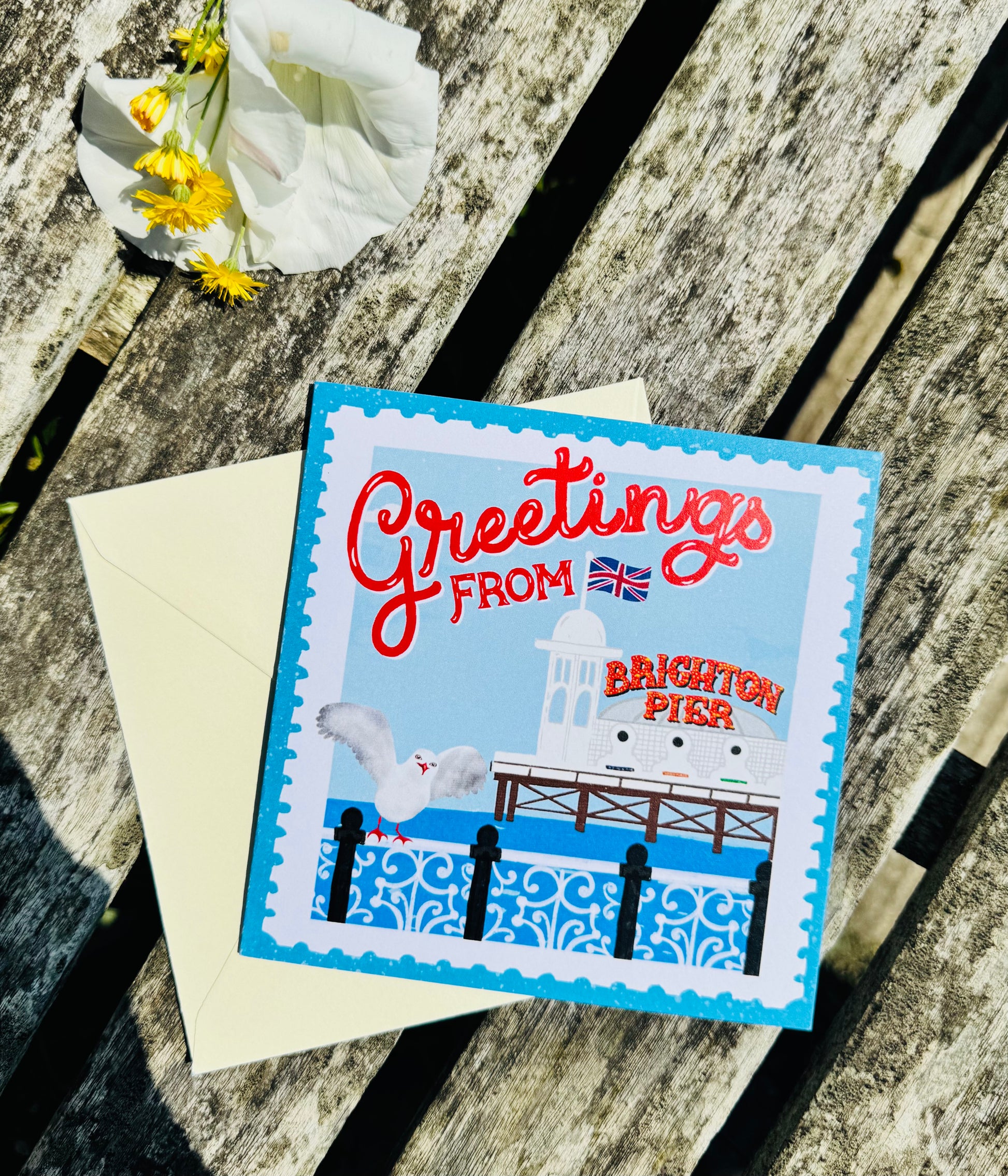 Greeting card with 'Greetings from Brighton Pier' text on a wooden surface with flowers.