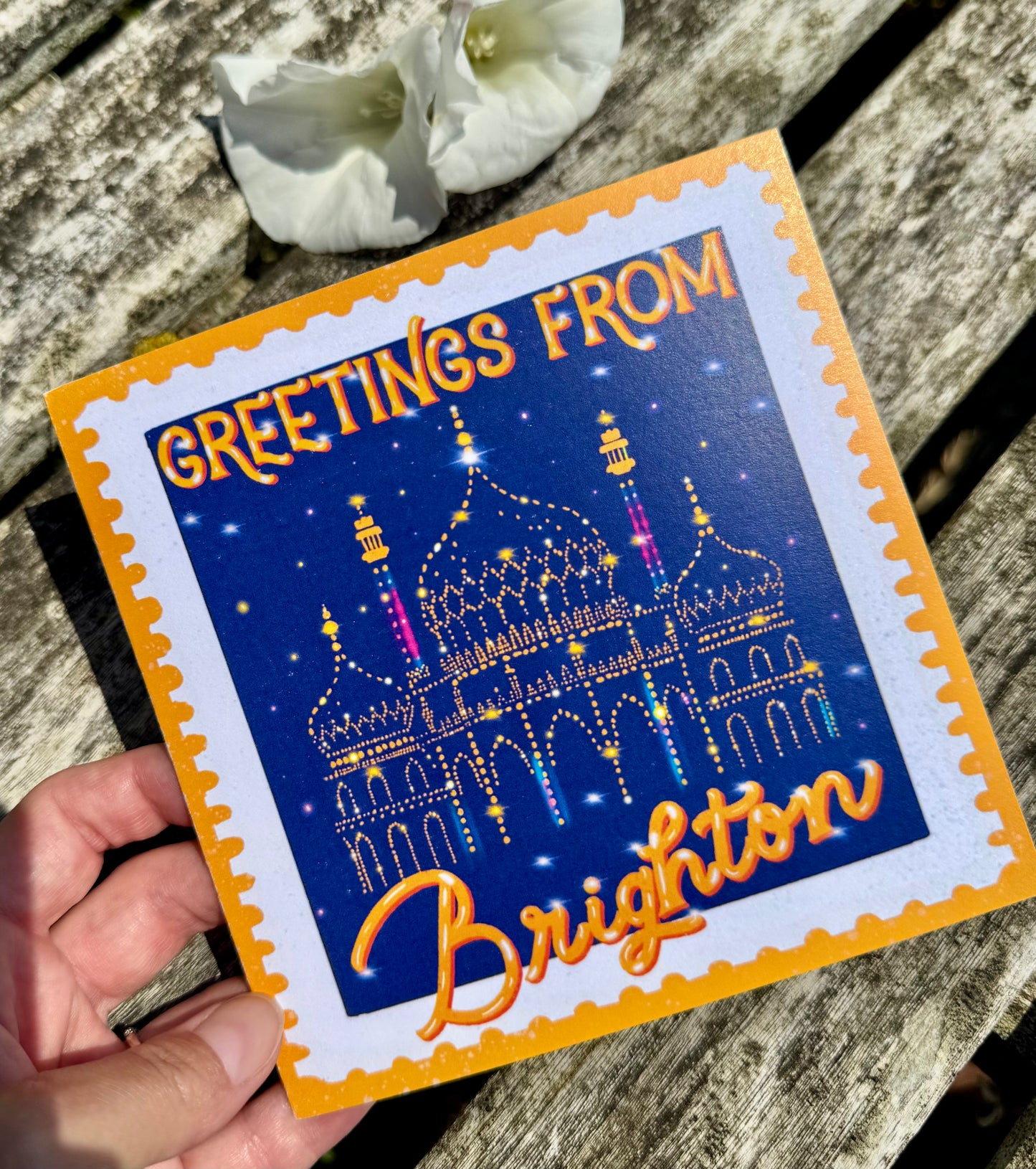 Greeting card with 'Greetings from Brighton' text and a colorful illustration of a building on a wooden surface.