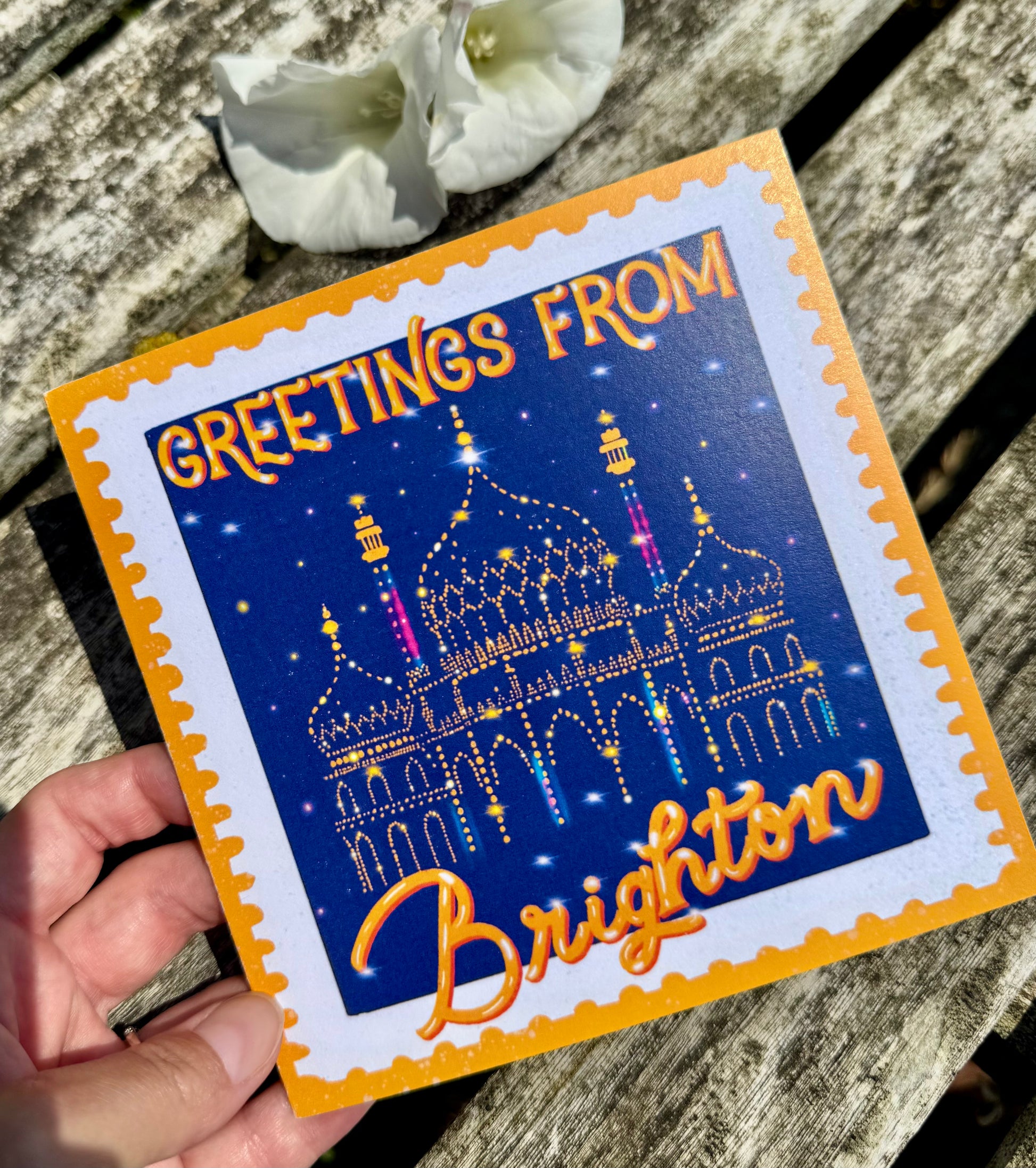 Greeting card with 'Greetings from Brighton' text and a colorful illustration of a building on a wooden surface.