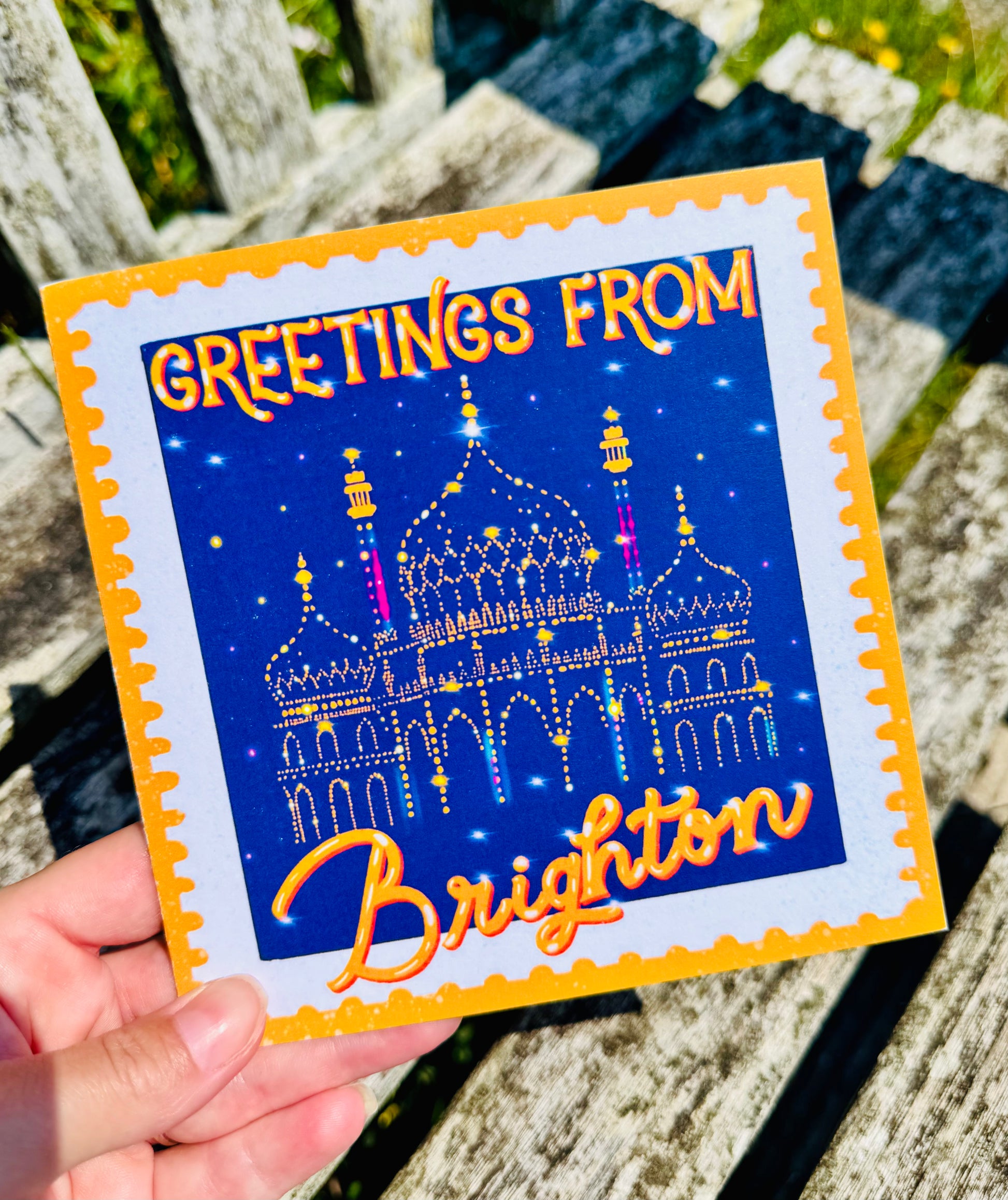 Greeting card with 'Greetings from Brighton' text and a castle illustration held by a hand.