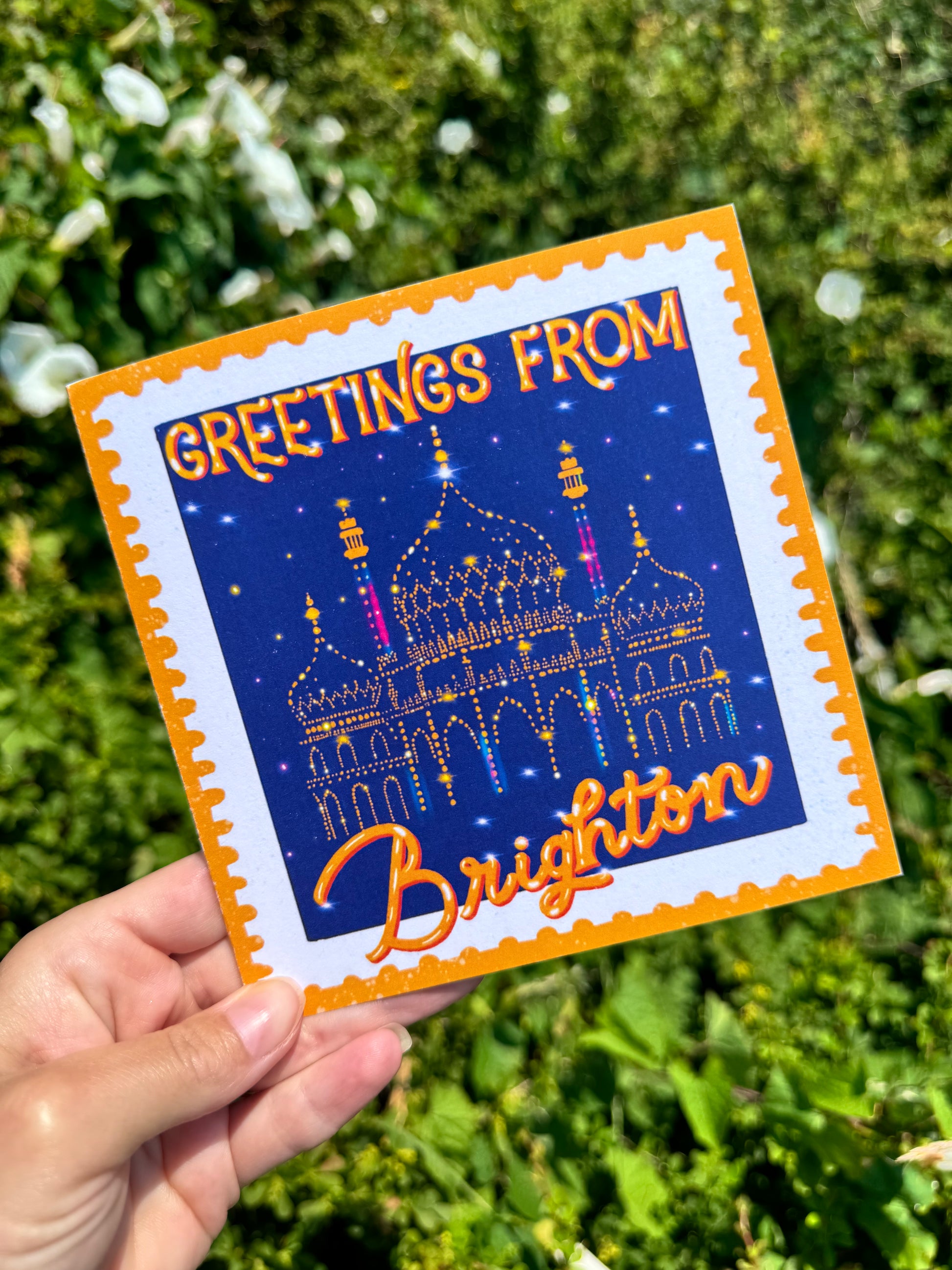 Card with 'Greetings from Brighton' text and a castle illustration held in front of green foliage.