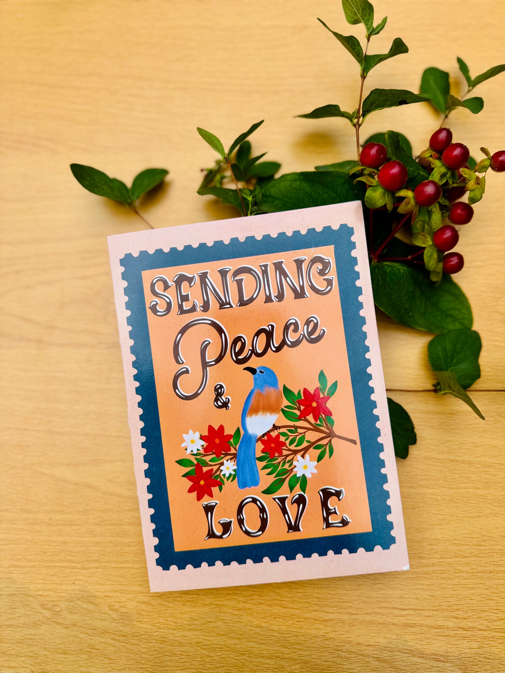 Card with 'Sending Peace & Love' text and a bird illustration on a wooden surface with greenery.