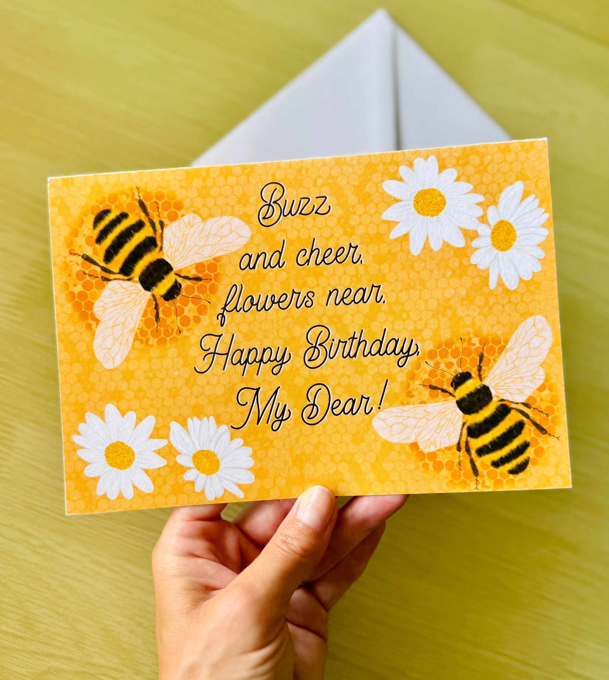 Hand holding a birthday card with bees and flowers on an orange background