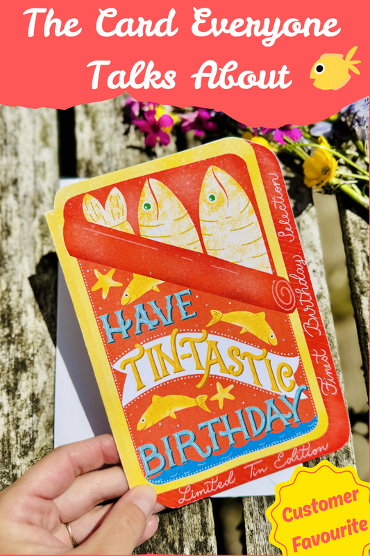 Birthday card with fish illustration held by a hand, against a natural background.