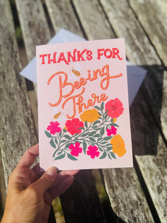 Hand holding a card with floral design and text on a wooden surface