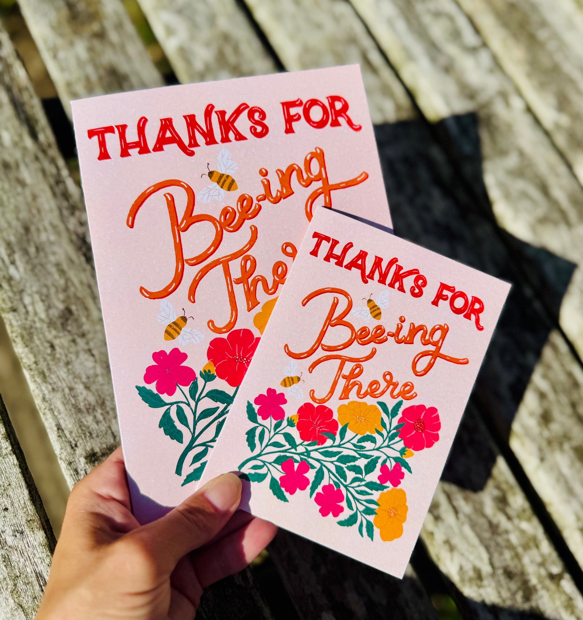Two greeting cards with floral designs and text on a wooden surface